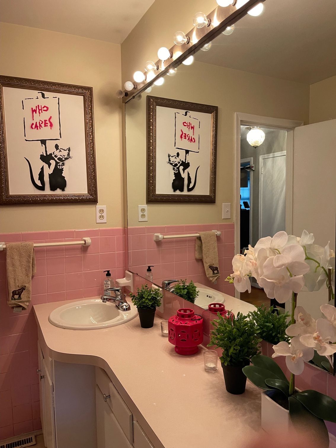 A bathroom with pink tiles , a sink , a mirror and two paintings on the wall.