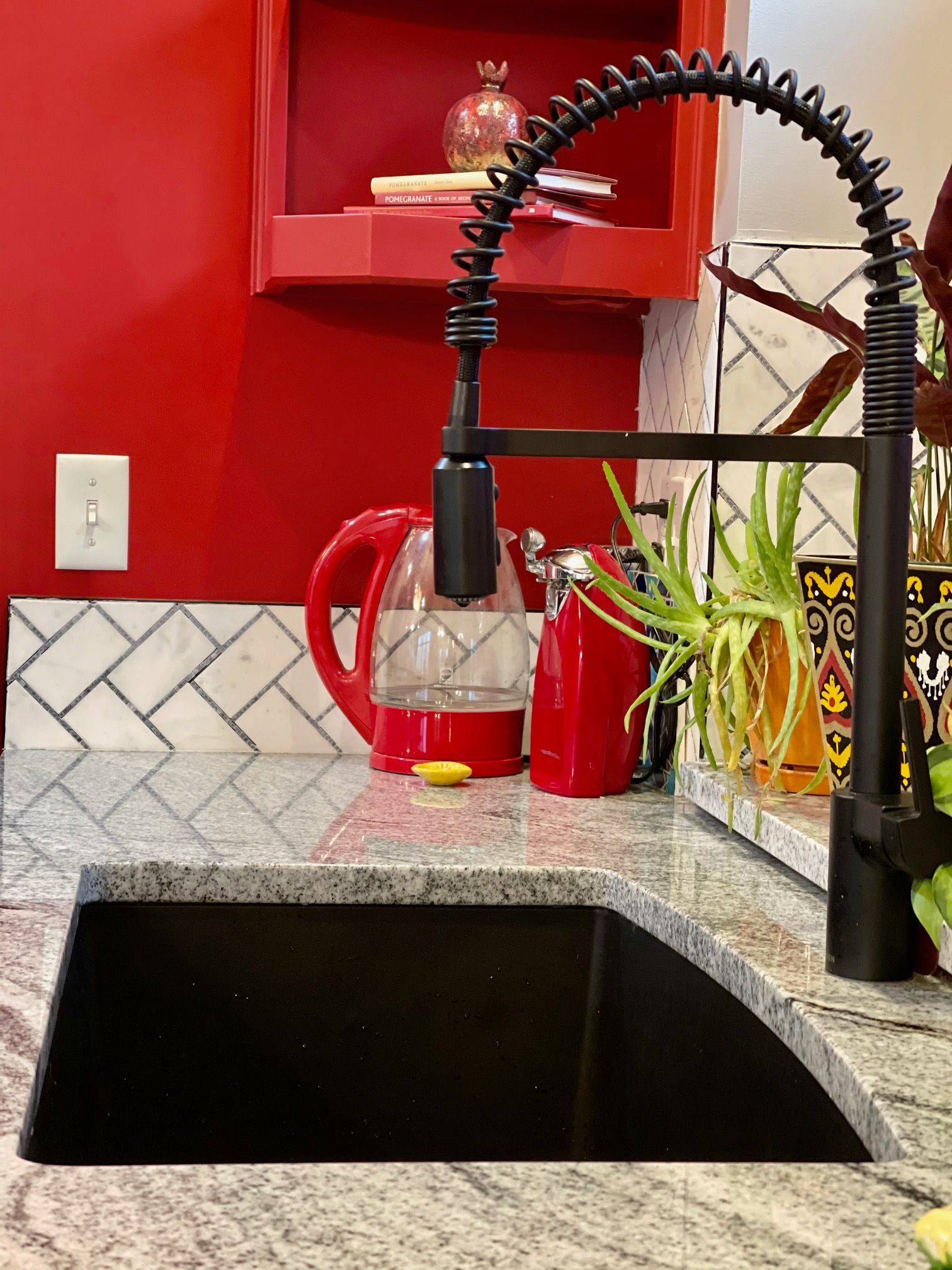 A kitchen sink with a black faucet and a red wall