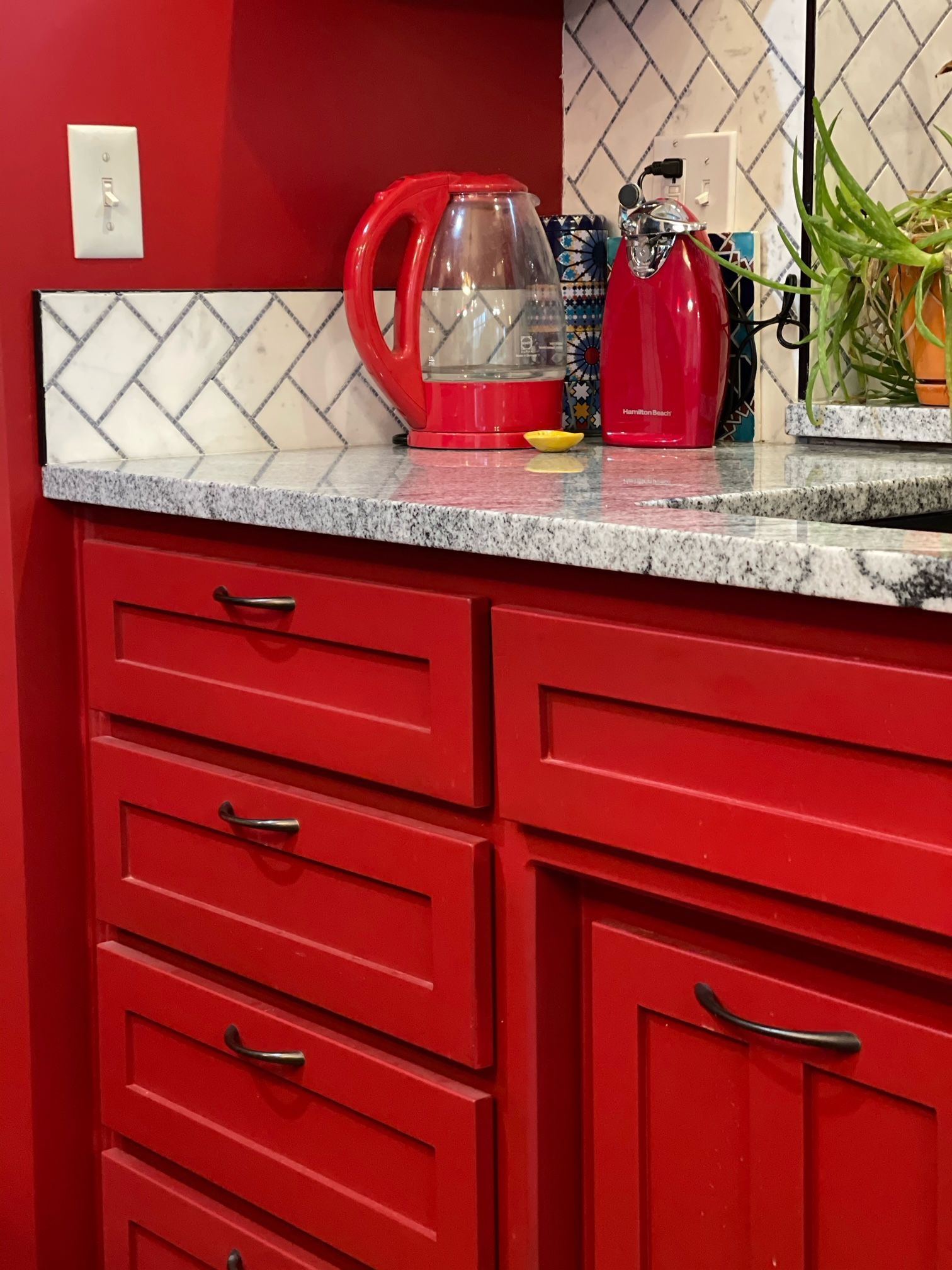 A kitchen with red cabinets and a red kettle on the counter.