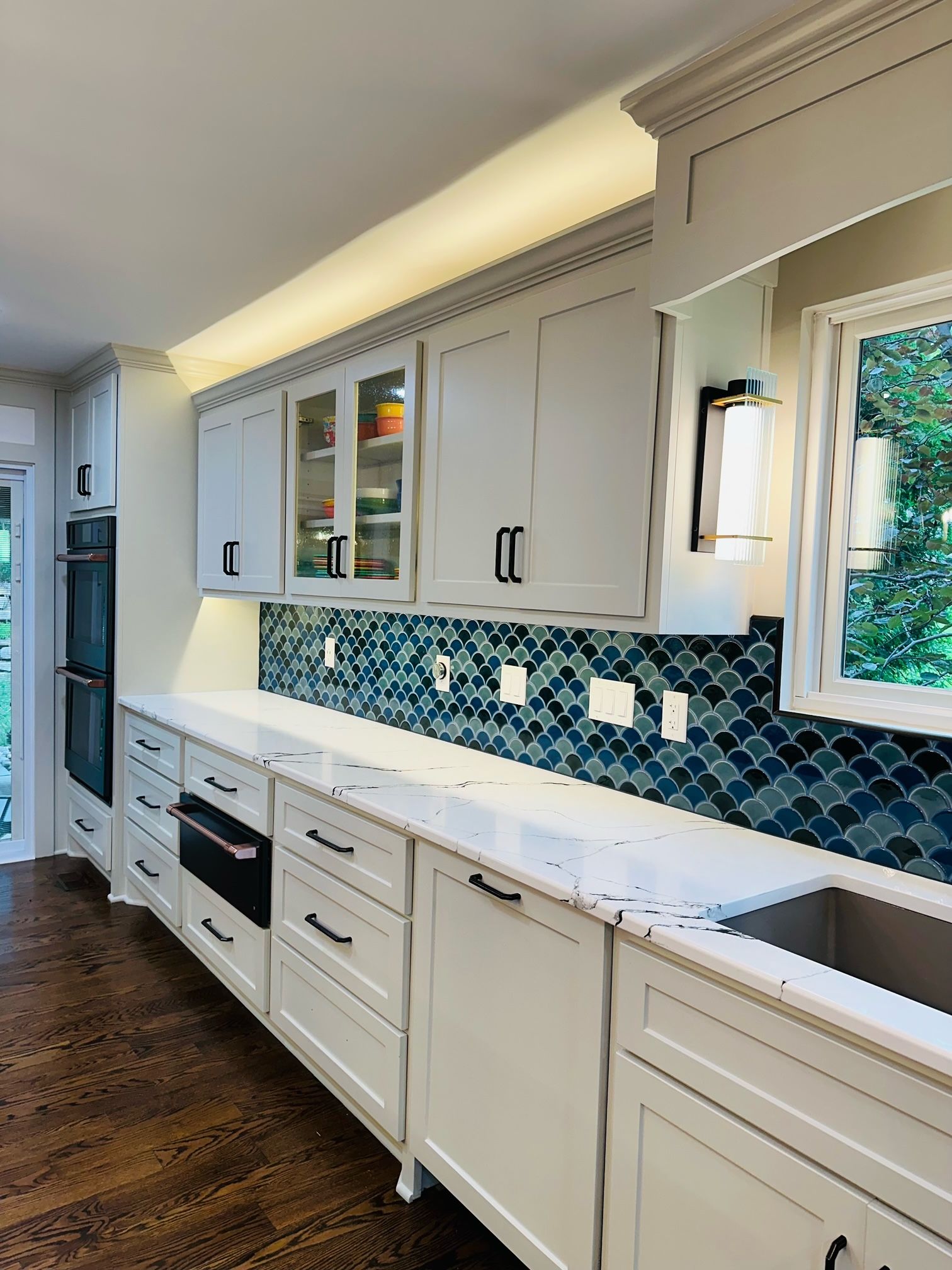 A kitchen with white cabinets , a sink , and a window.