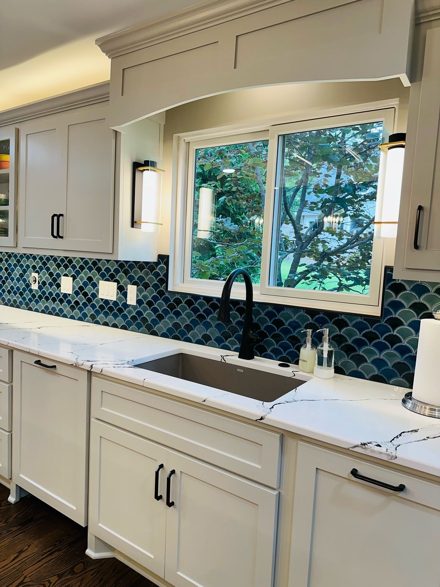 A kitchen with white cabinets , a sink , and a window.