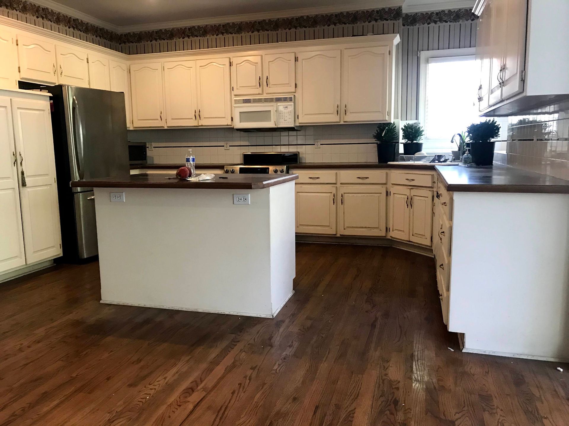 A kitchen with white cabinets and hardwood floors has a large island in the middle.