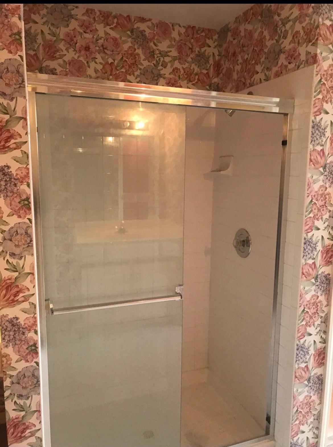 A bathroom with a sliding glass shower door and floral wallpaper.