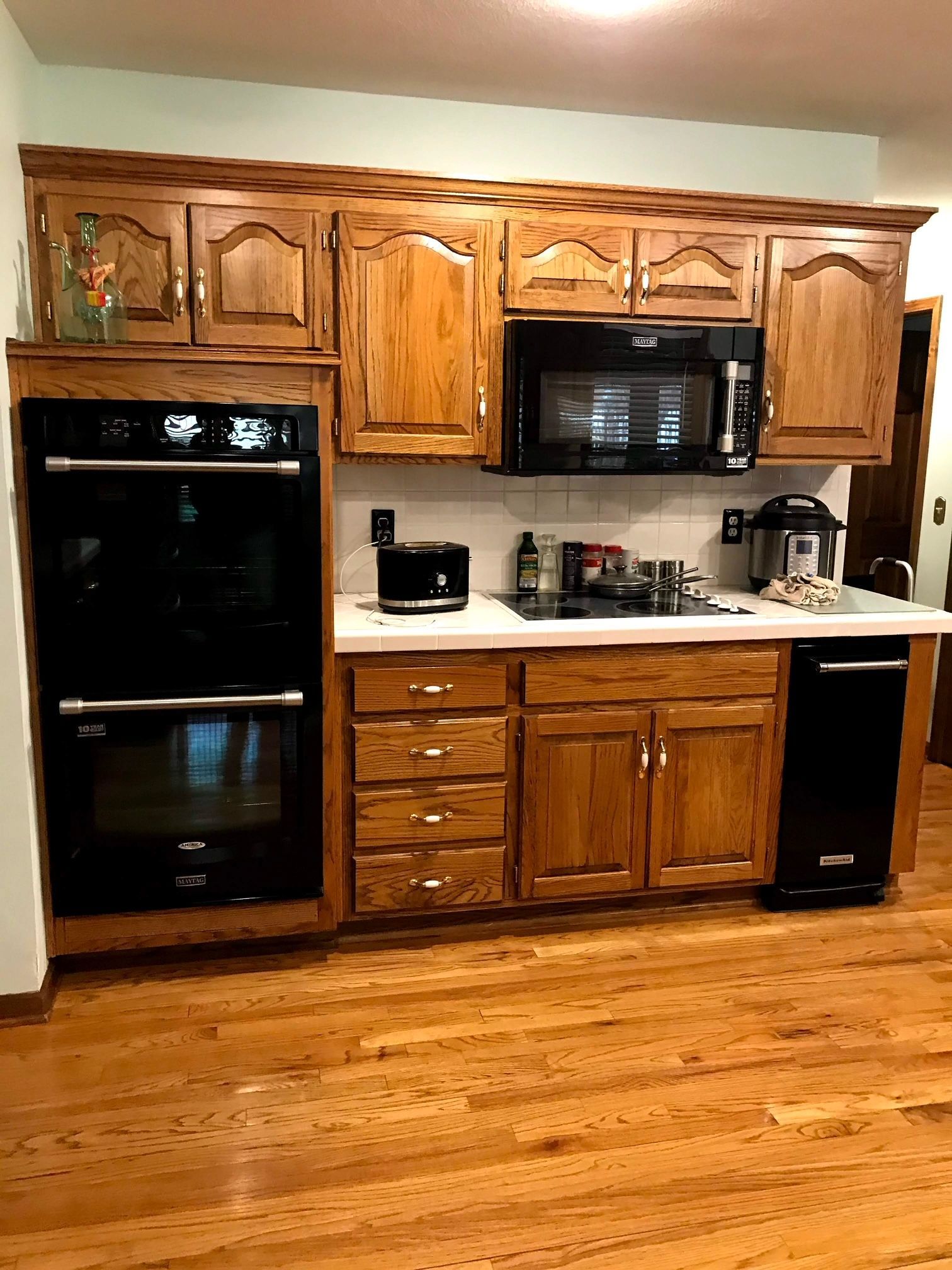 A kitchen with wooden cabinets , black appliances , and hardwood floors.