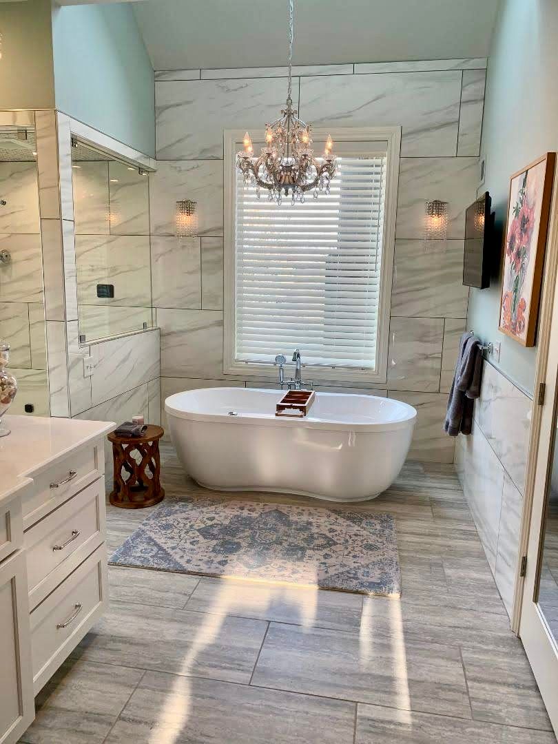 A bathroom with a bathtub , sink , mirror and chandelier.