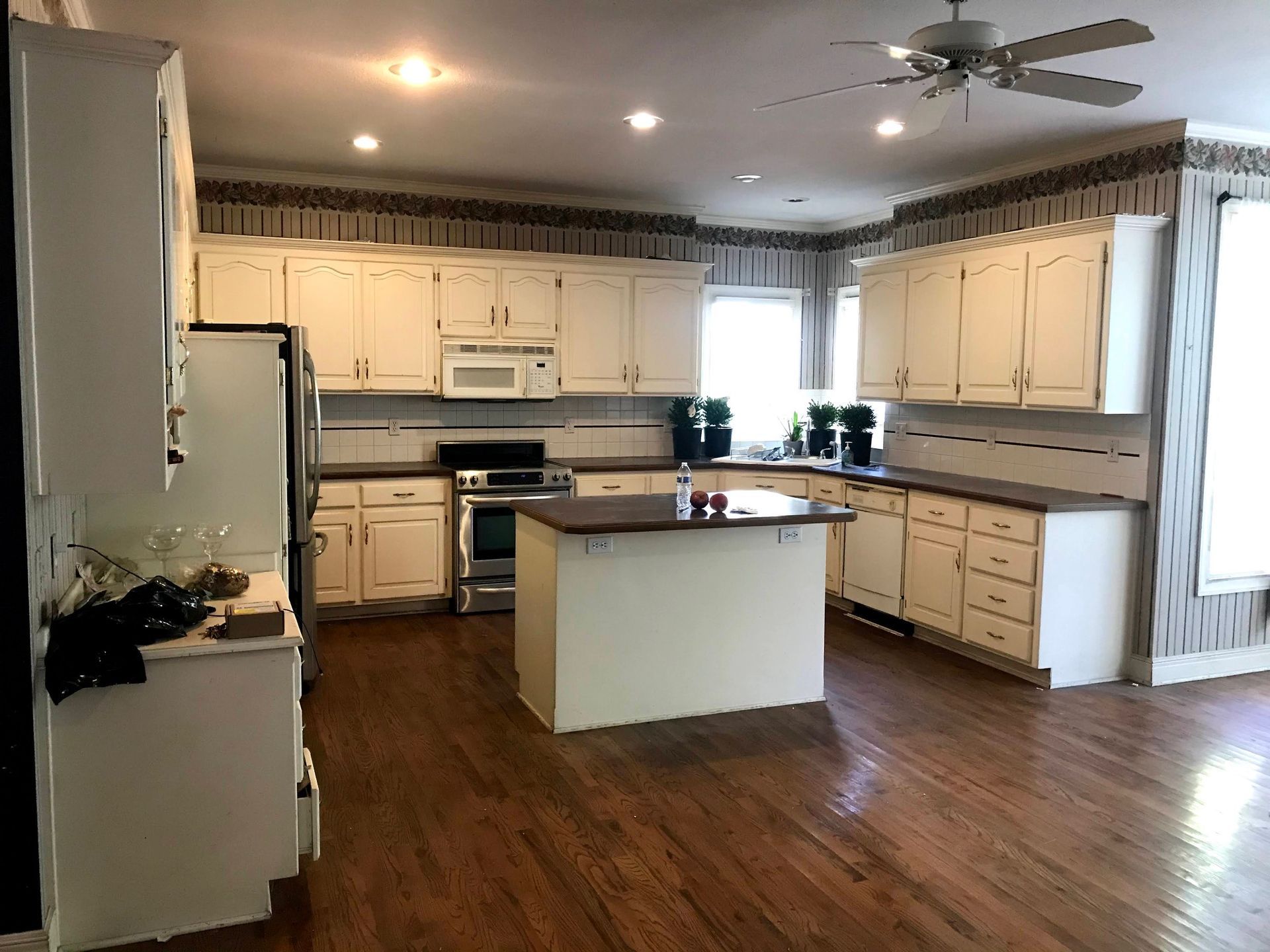 A kitchen with white cabinets , hardwood floors , a stove and a ceiling fan.