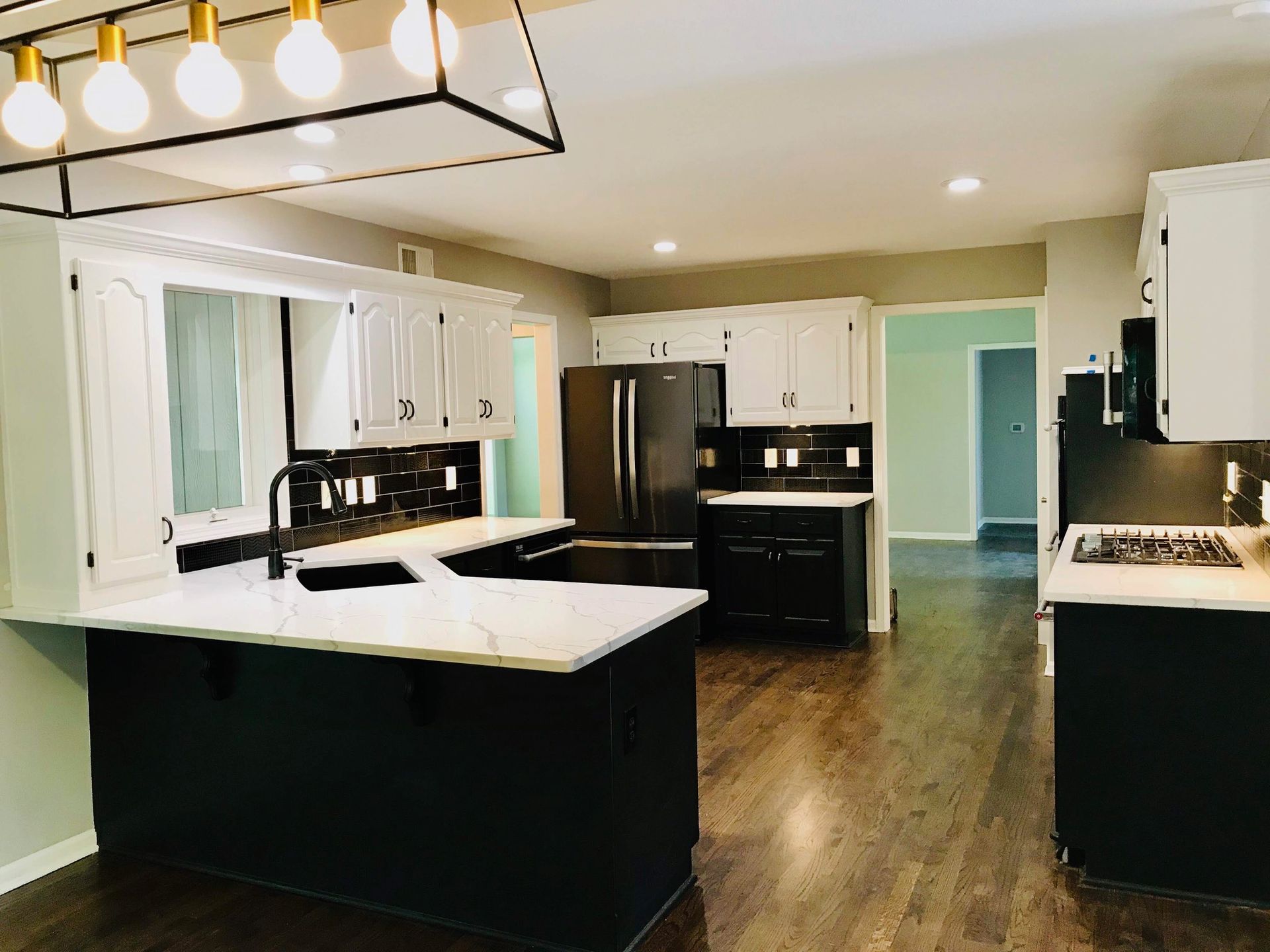 A kitchen with black cabinets , white cabinets , stainless steel appliances and a large island.