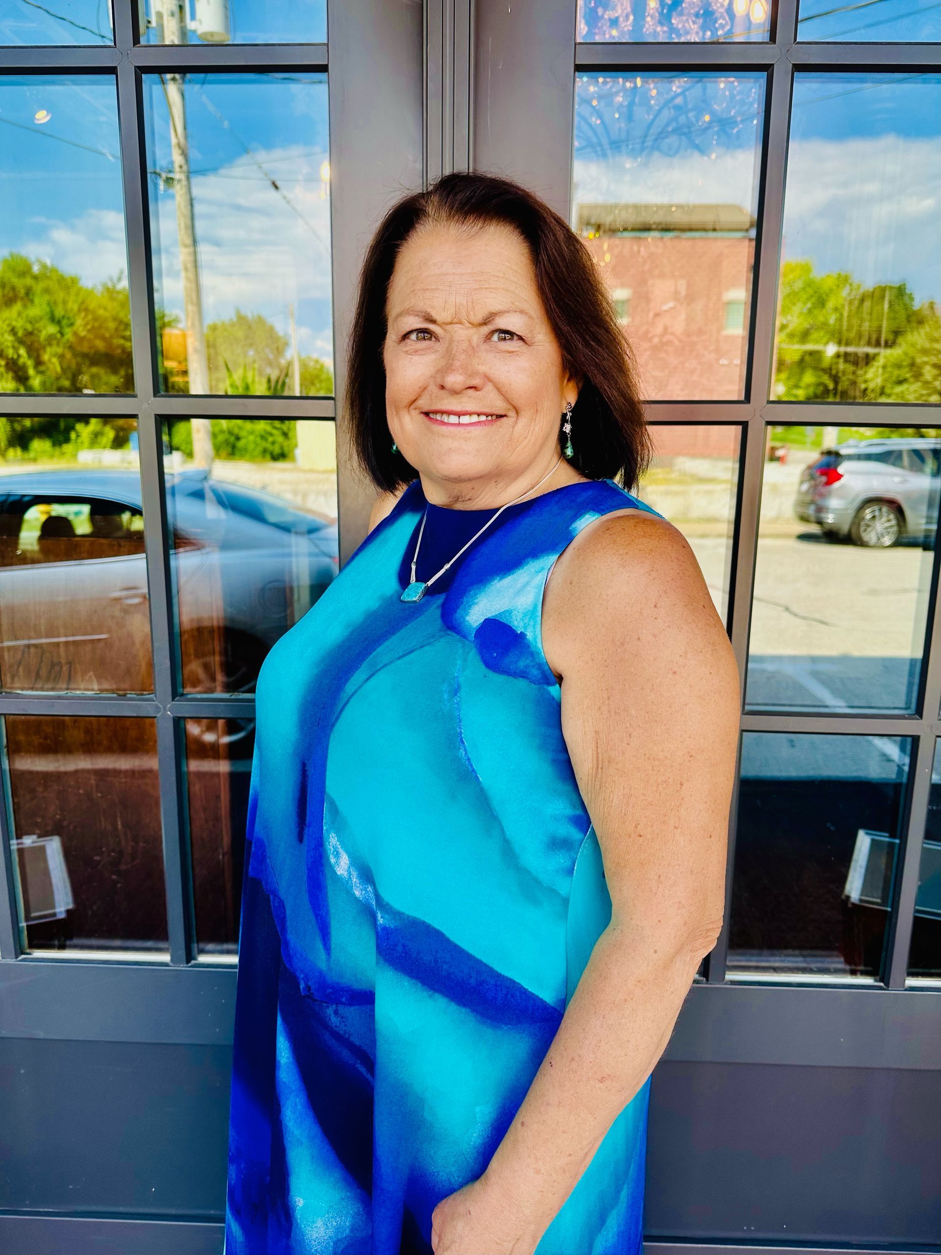 A woman in a blue dress is standing in front of a building.