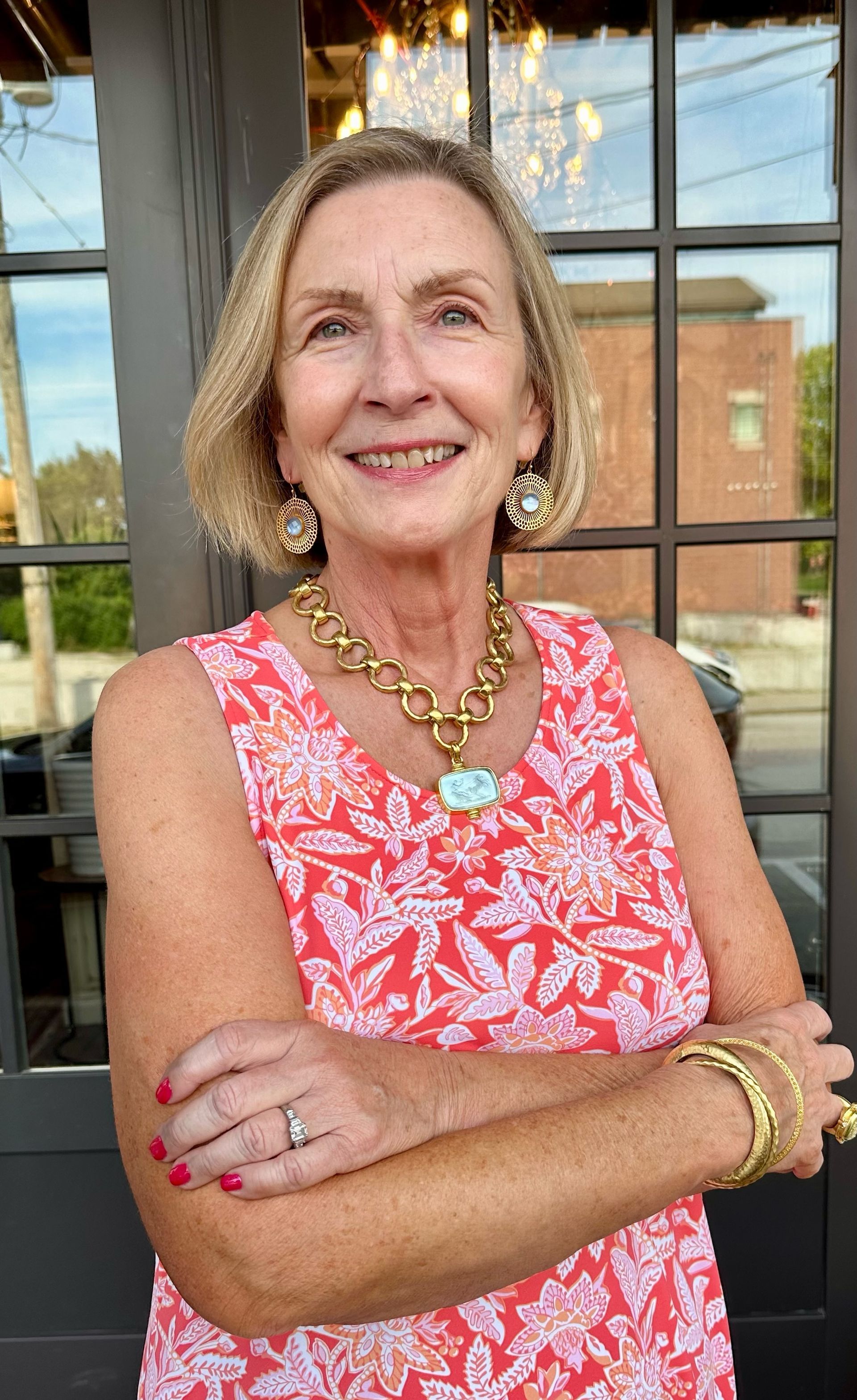 A woman in a red dress is standing with her arms crossed and smiling.