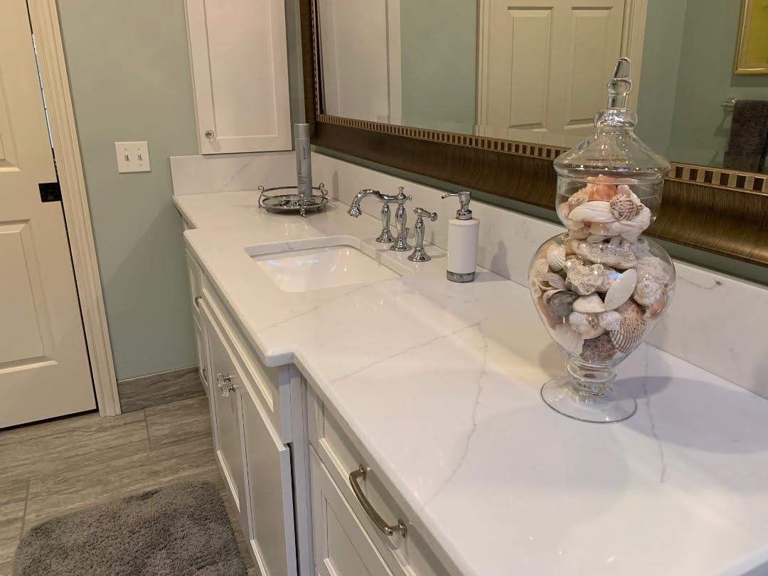 A bathroom with two sinks , a mirror and a vase of seashells on the counter.
