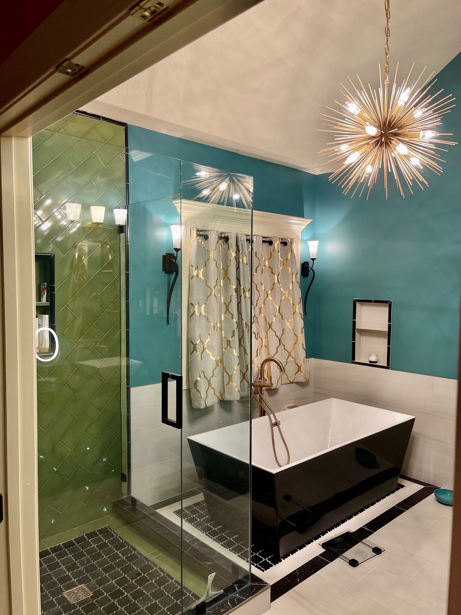 A bathroom with a black tub , shower , and chandelier.