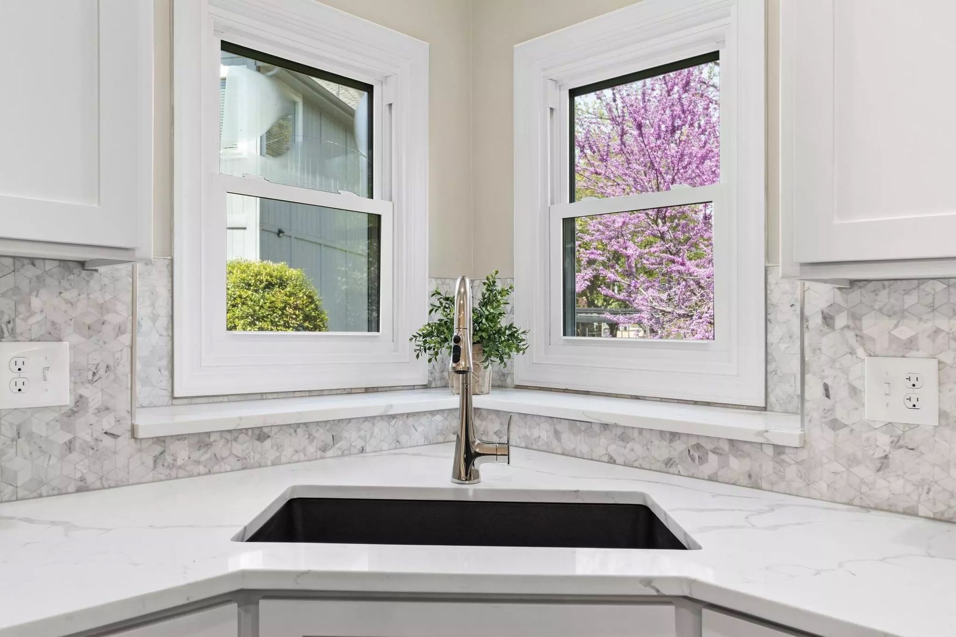 A kitchen sink in the corner of a kitchen with two windows.
