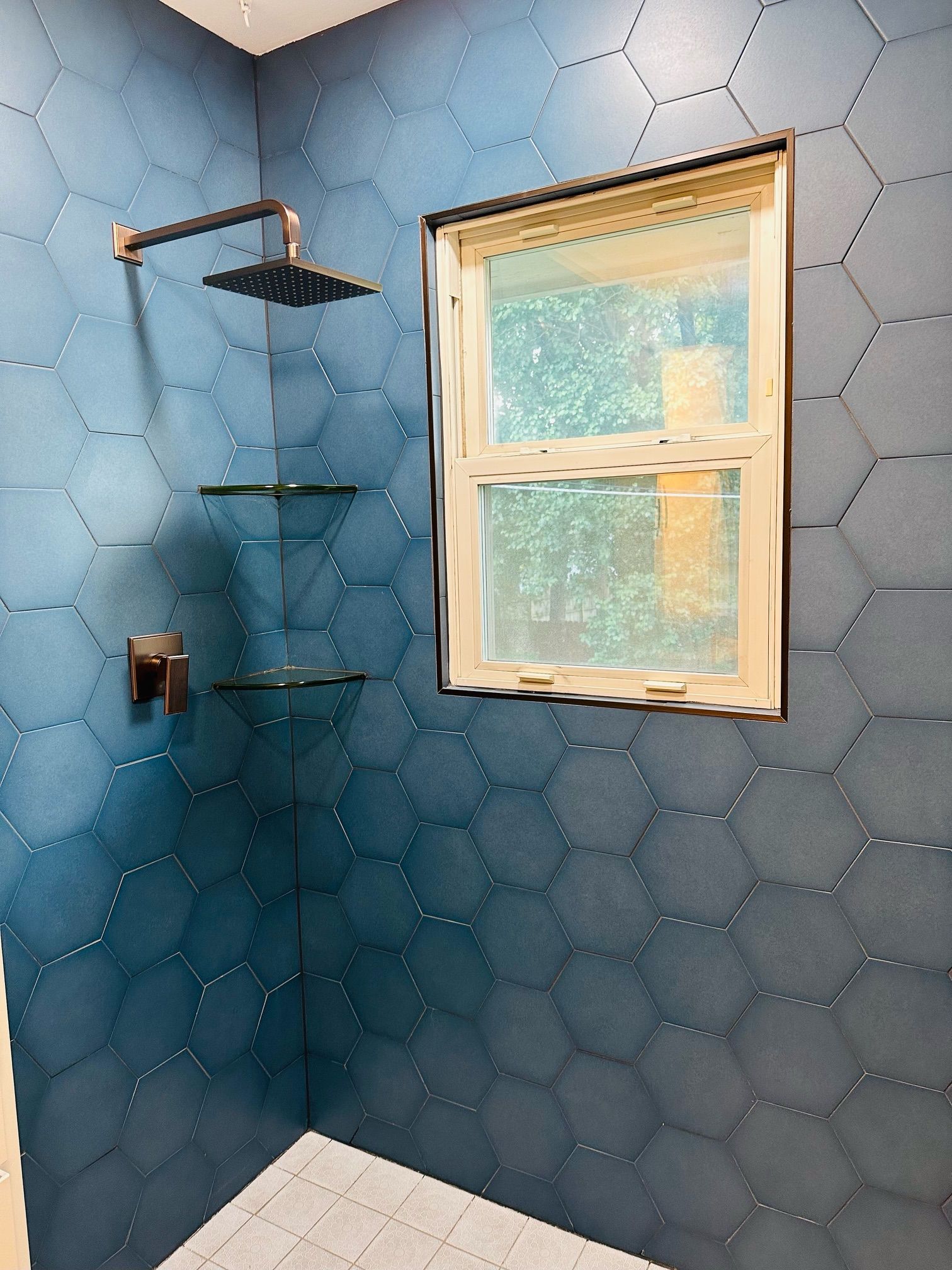 A bathroom with blue tiles , a shower head and a window.