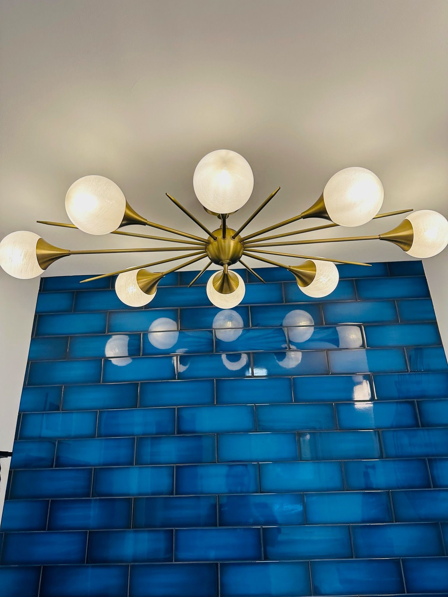 A chandelier is hanging from the ceiling above a blue tiled wall.