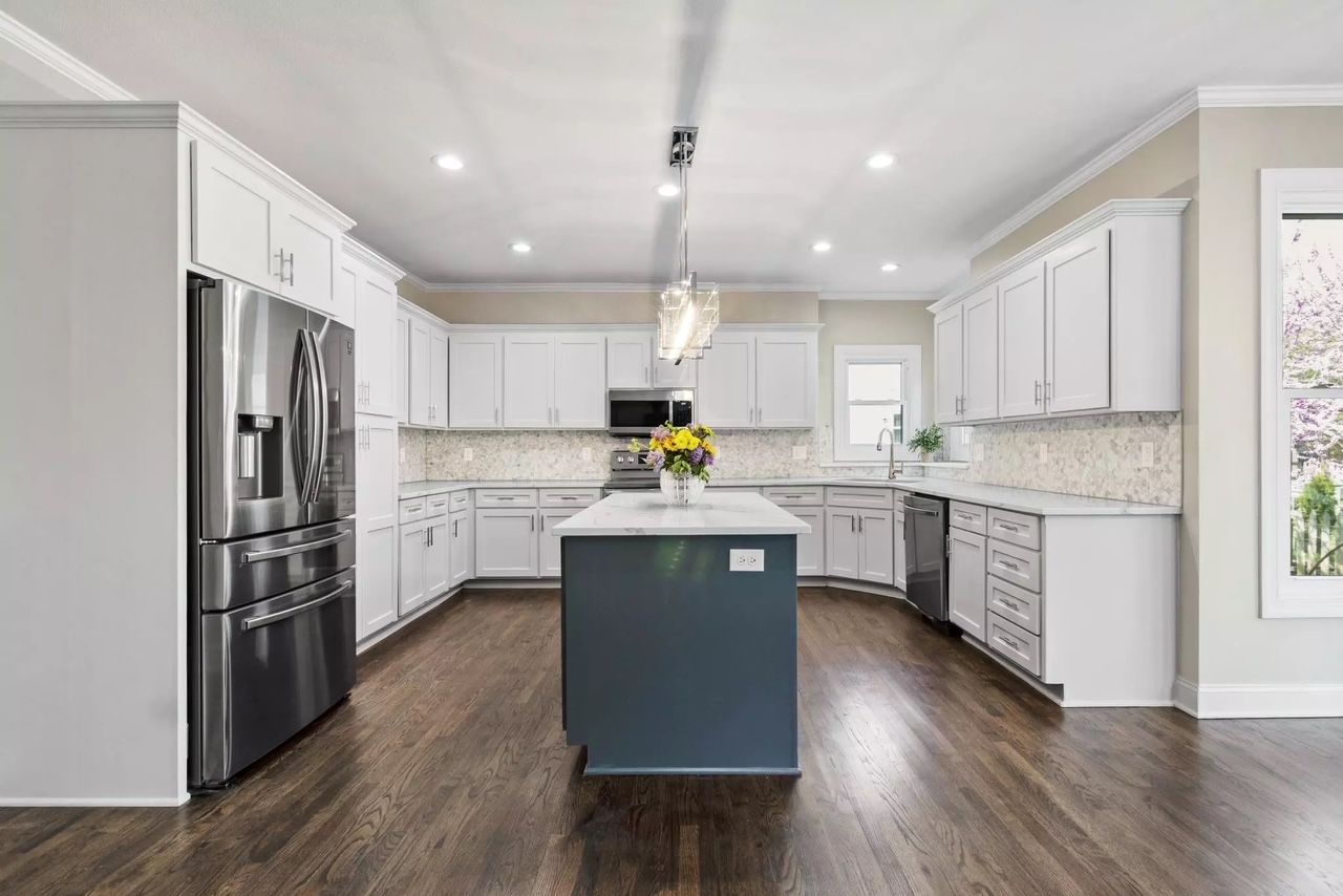 A kitchen with white cabinets , stainless steel appliances , and a large island.
