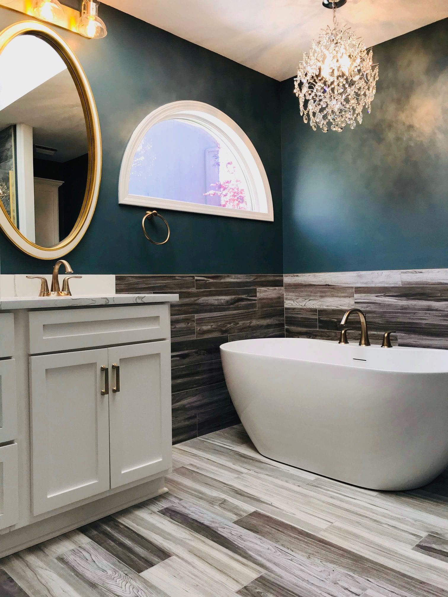 A bathroom with a tub , sink , mirror and chandelier.