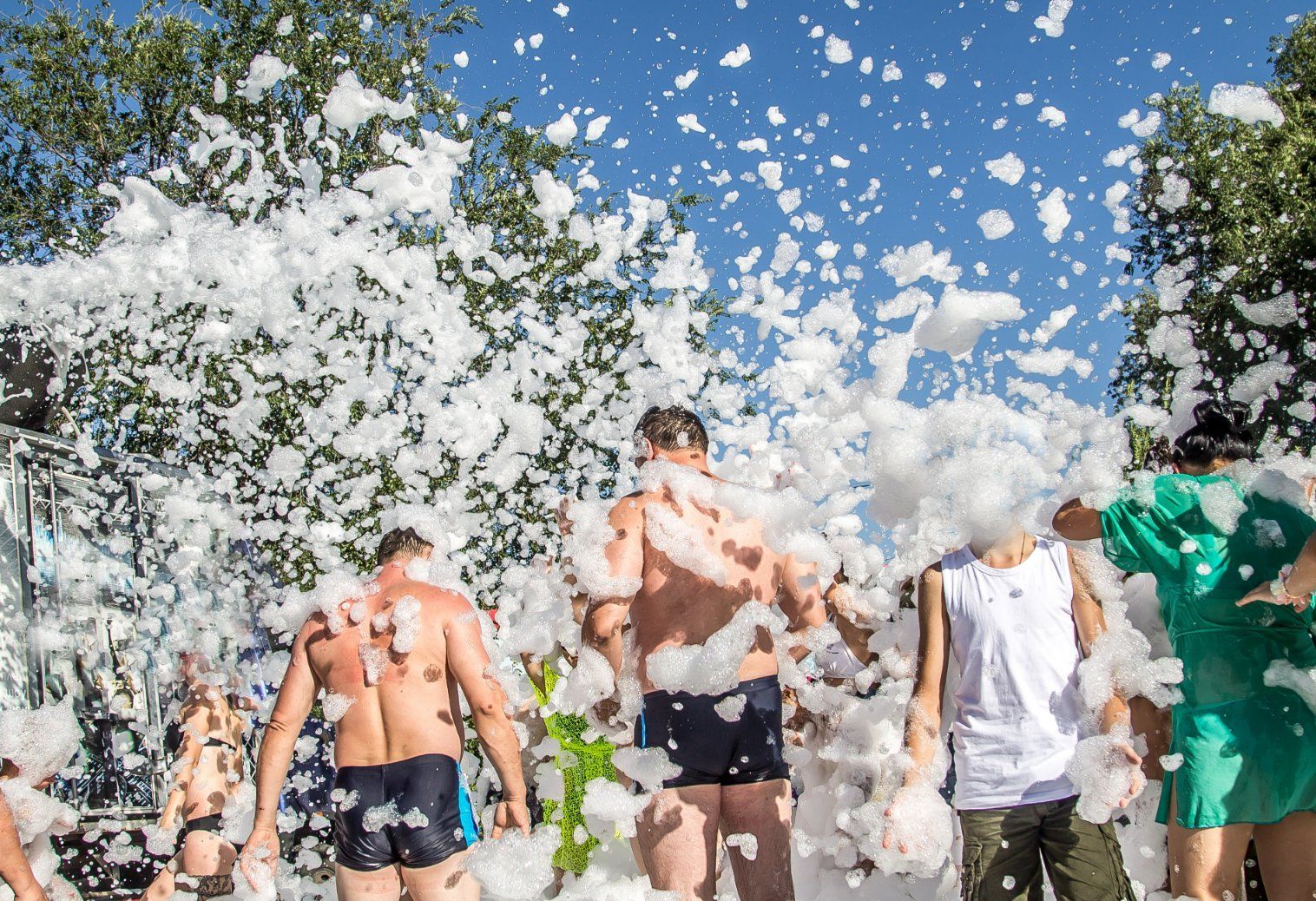 People in swimwear at outdoor foam party, blue sky.
