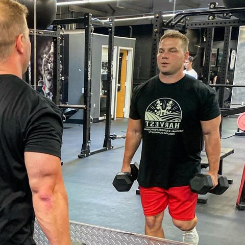 a man lifting dumbbells in a gym wearing a shirt that says t23v8ah