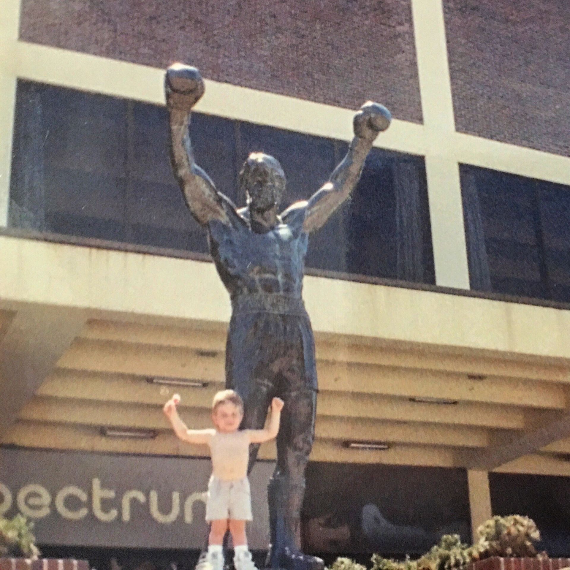 A little boy stands in front of a statue of rocky balboa
