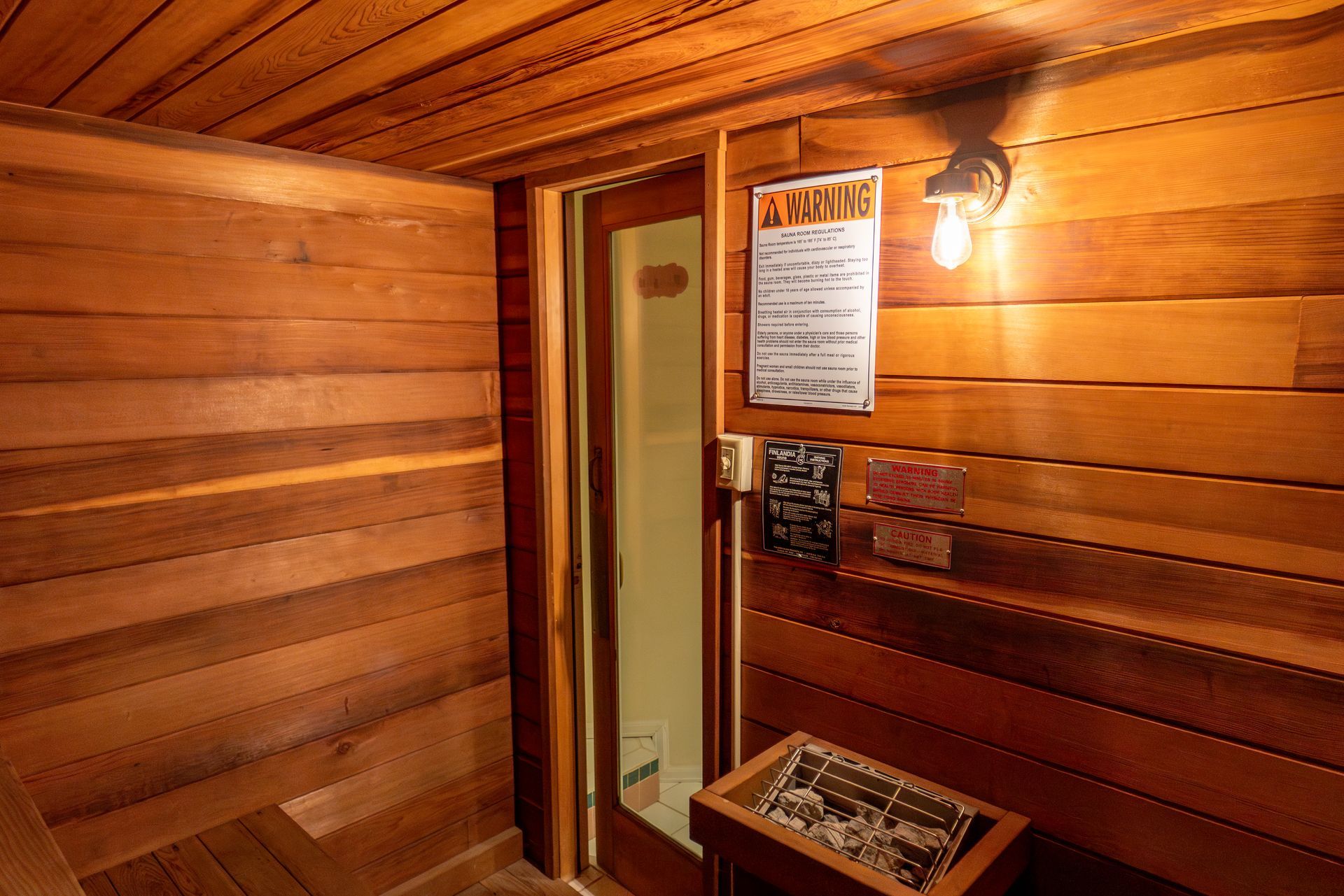 A wooden sauna with a glass door and a warning sign on the wall.