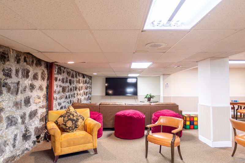 A living room with a couch , chairs , ottomans and a television.