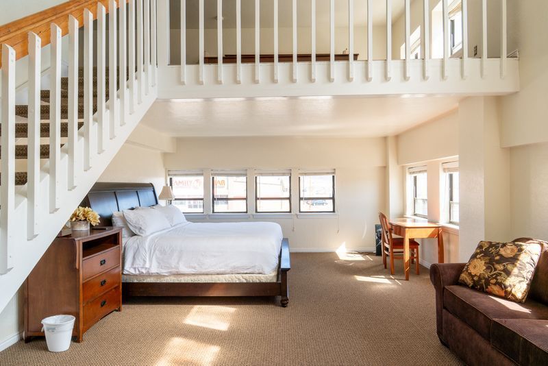 A bedroom with a bed , couch , desk and stairs.