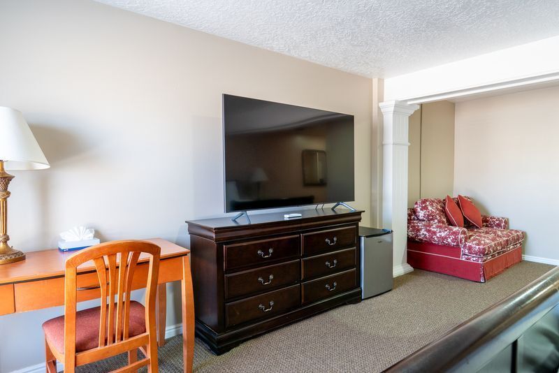 A hotel room with a flat screen tv , dresser , desk , chair and couch.