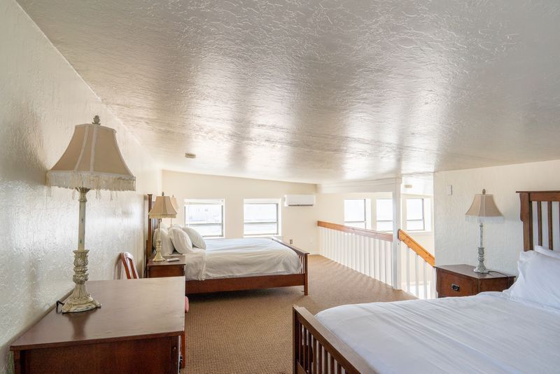 A hotel room with two beds , a nightstand , lamps and a staircase.