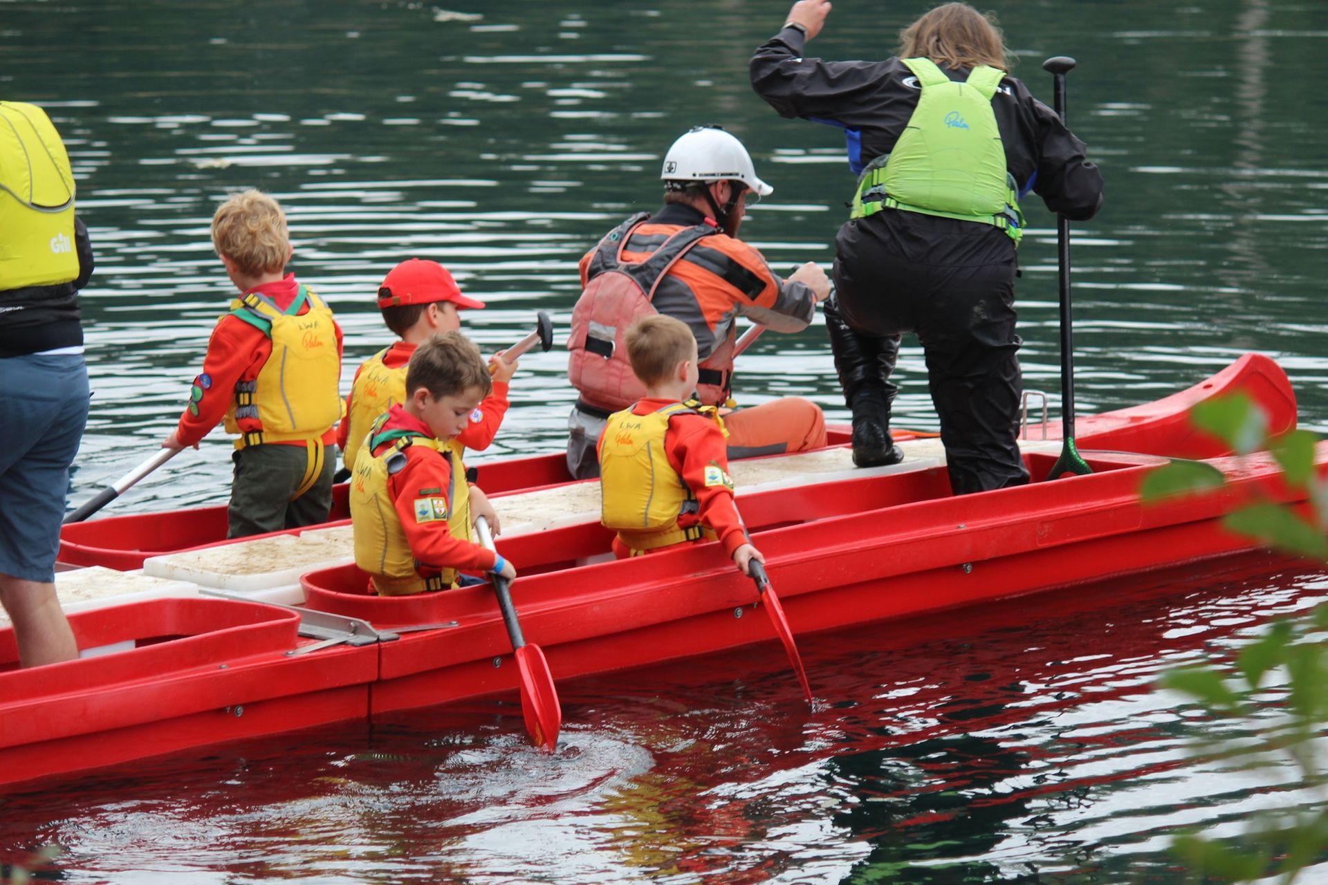 Squirrels in life jackets paddling a red canoe on the lake during water activities at camp.