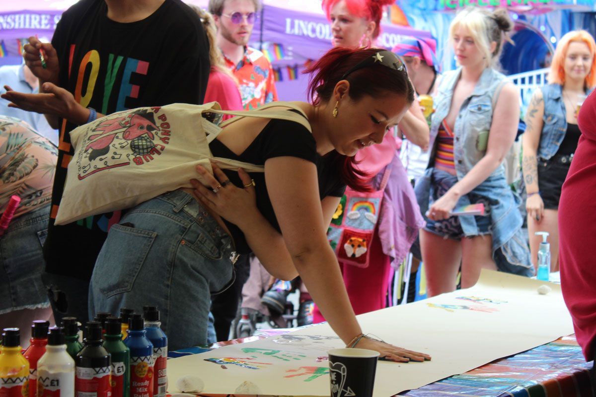 Adding a rainbow handprint to our Pride wall. An attendee at Lincoln Pride 2025 presses their painted hand onto the Scouts handprint wall activity.
