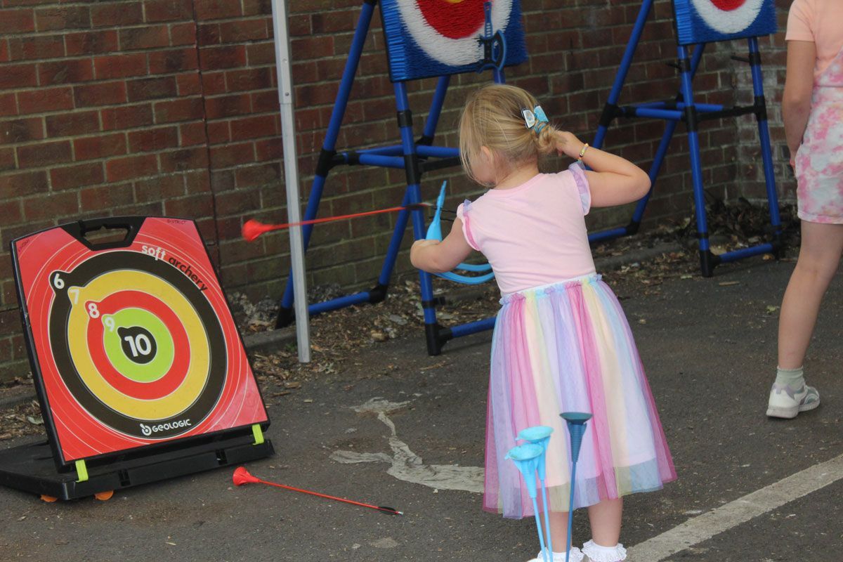 A little one having a go at soft archery in the Family Zone. A young child in a rainbow skirt takes aim with a soft archery bow at Lincoln Pride Family Zone.
