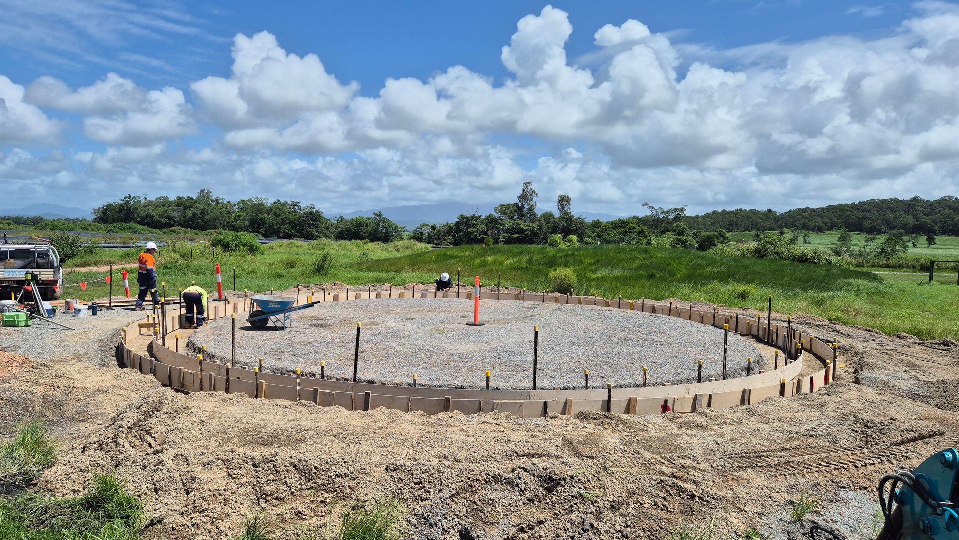 Construction site with circular concrete foundation, workers, rebar, and blue sky over grassy field — King Reef Concrete in Kurrimine Beach, QLD