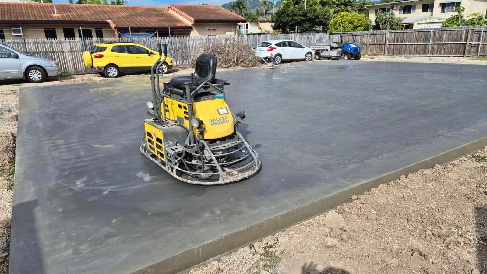 Yellow compacting machine smoothing a large concrete slab at a construction site