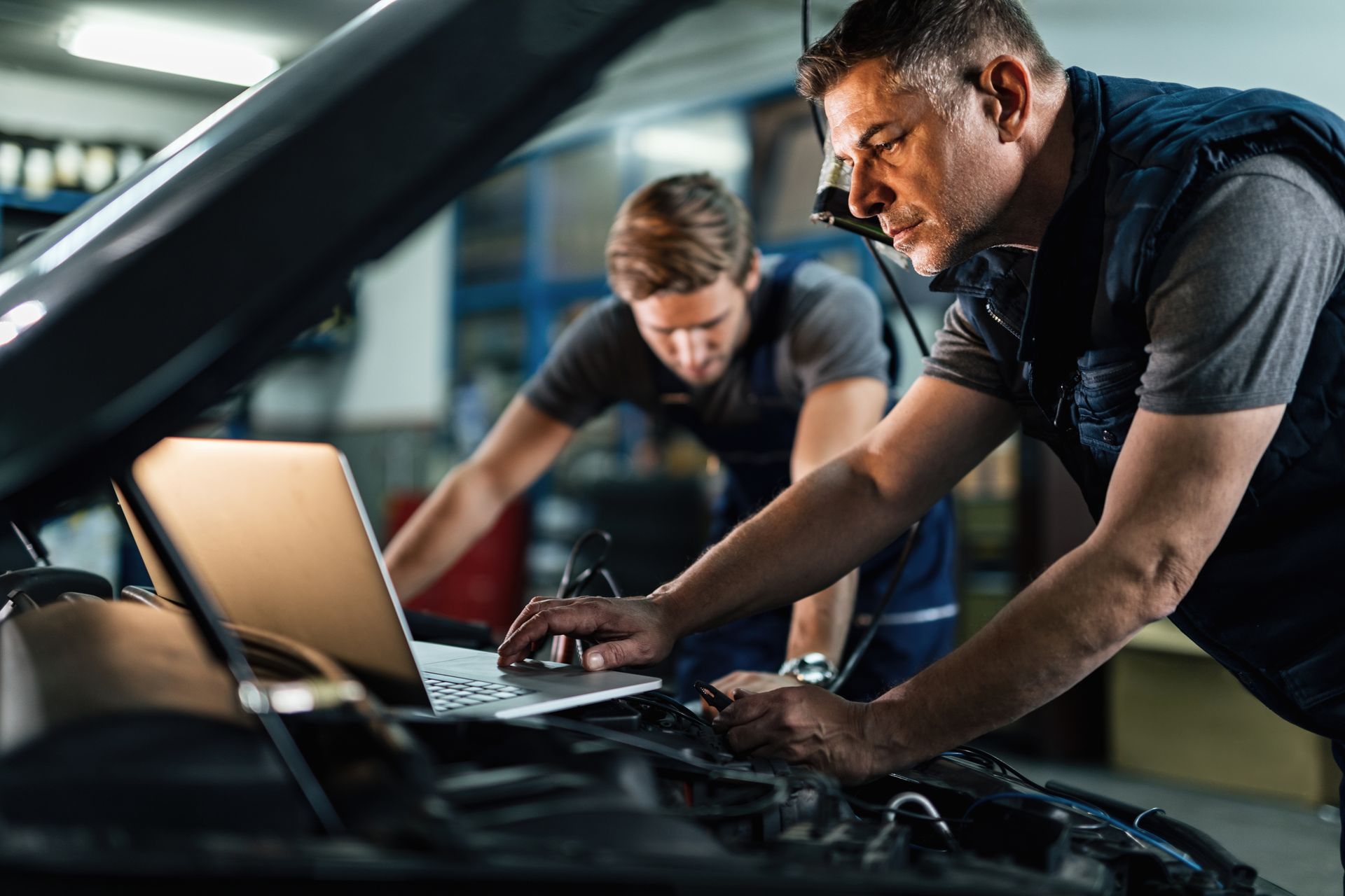 Auto mechanic using a laptop while working on a car diagnostic with his coworker.