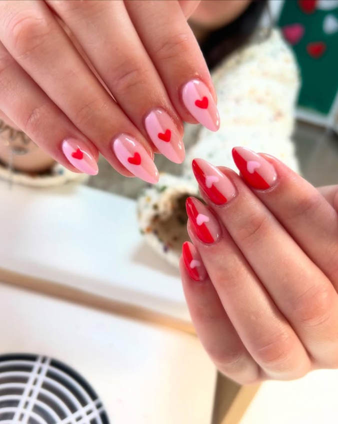 Manos de una persona con uñas en forma de almendra pintadas de rosa y rojo con detalles de corazones, celebrando el día de San Valentín.