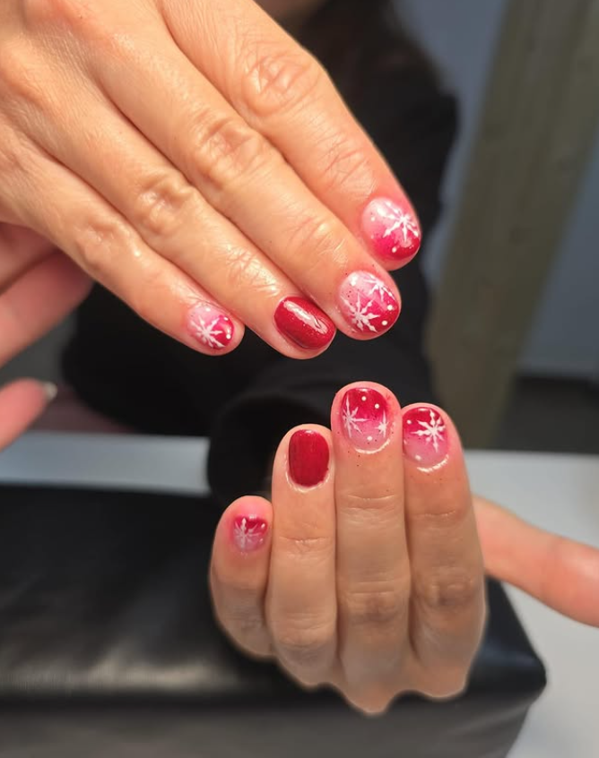 Arte de uñas en rojo y blanco con diseño de copo de nieve, un degradado degradado en algunas uñas.