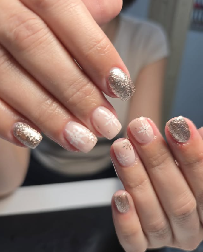 Primer plano de manos con un diseño de uñas neutro y brillante. Uñas con detalles de purpurina dorada y delicados detalles de copos de nieve blancos.