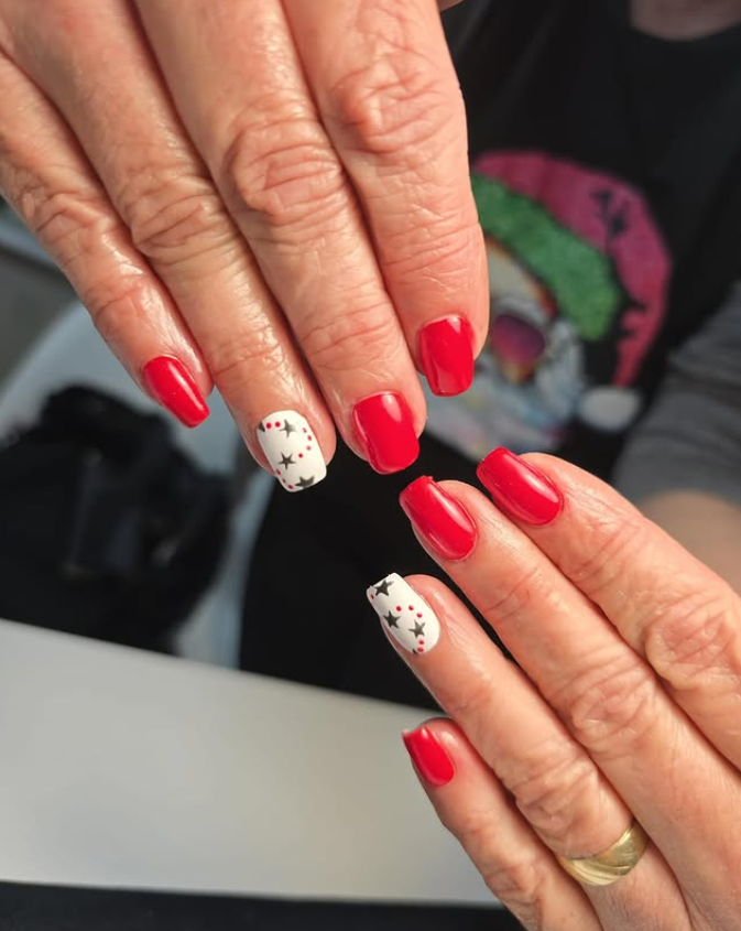 Manos con esmalte de uñas rojo, una uña en cada mano pintada de blanco con detalles de estrellas negras.