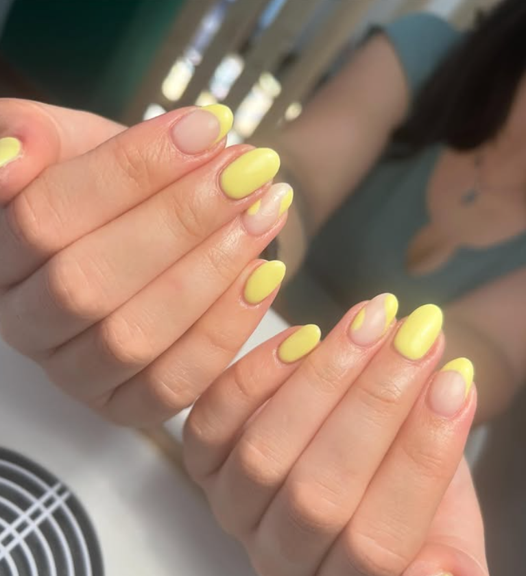 Manos con uñas amarillas ovaladas. Algunas tienen puntas francesas, otras tienen manchas amarillas.