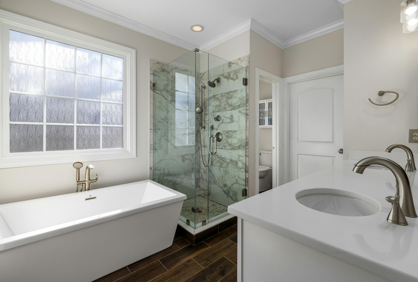 A bright, modern bathroom featuring a white soaking tub, a glass-enclosed shower, and a vanity with a white countertop.