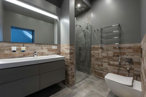Modern bathroom with a wall-mounted vanity, gray cabinets, stone-tiled walls, a walk-in shower, and a white toilet.