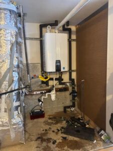 A wall-mounted tankless water heater with black PVC piping and a condensate pump on the floor, in a utility space.