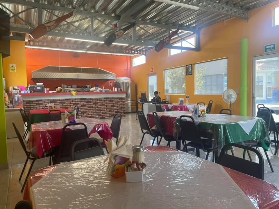 An empty restaurant interior with tables covered in plastic tablecloths, bright orange walls, and a service counter.