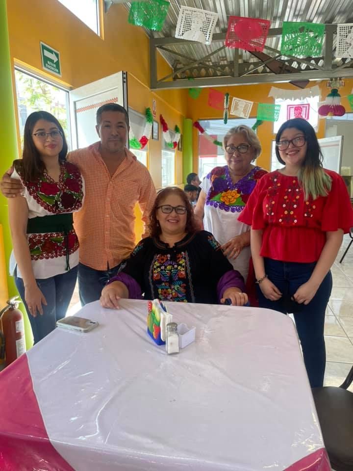 Five people stand and sit in a room decorated with colorful banners, posing for a photo behind a table with a white cloth.
