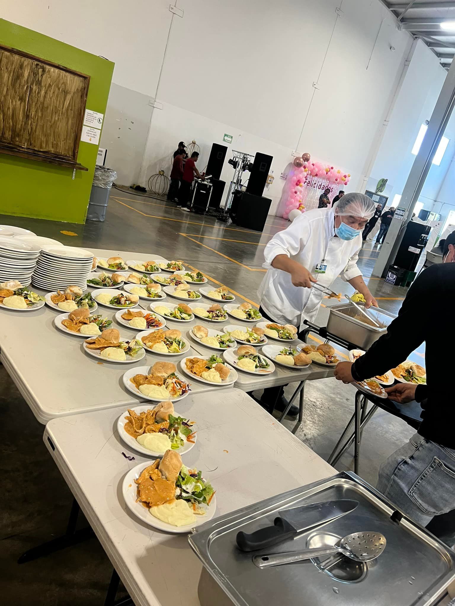 A chef serving plated meals from a long buffet table in a large warehouse-style venue.