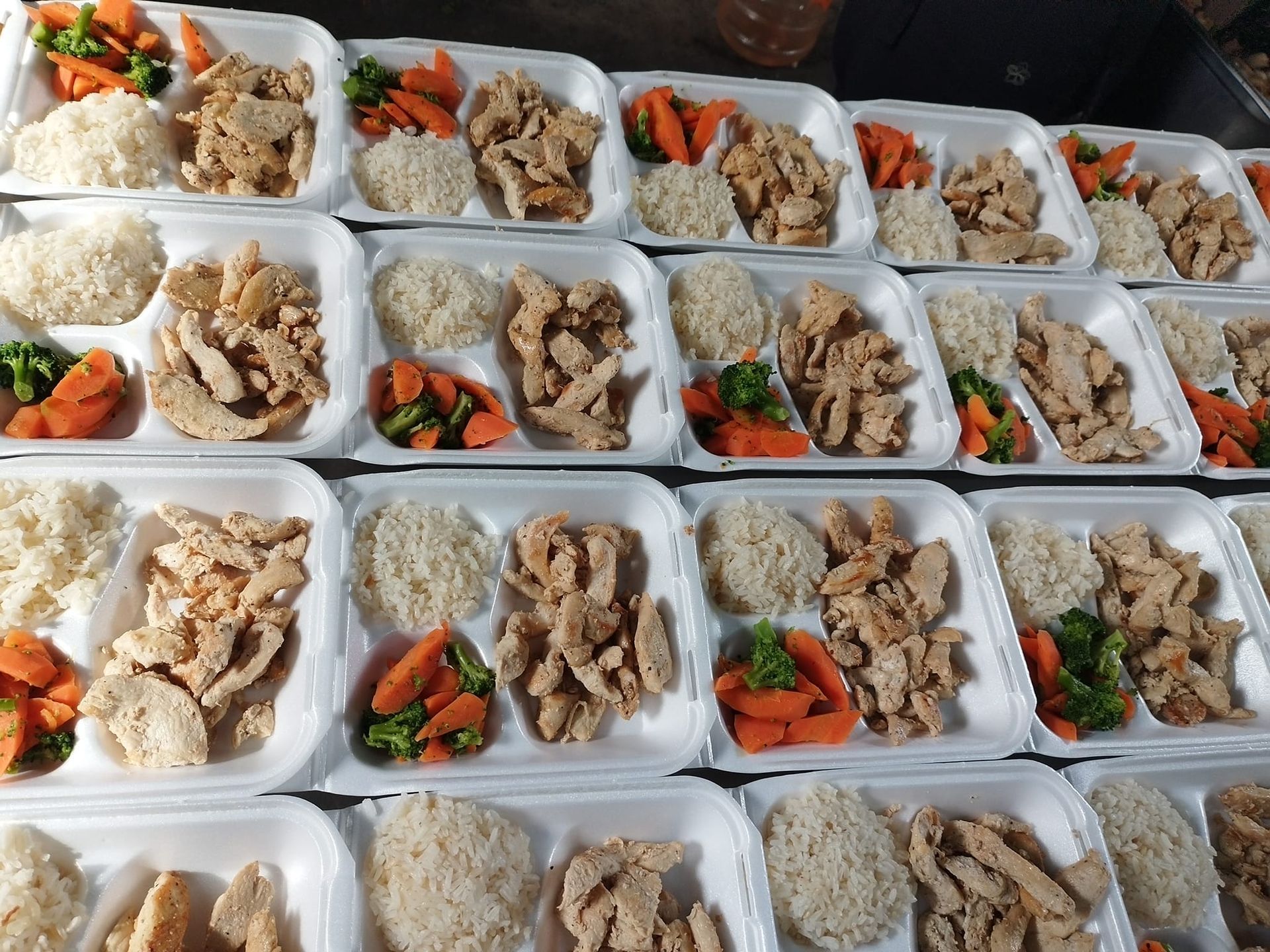 Rows of white takeout containers filled with portions of chicken, white rice, and steamed vegetables.