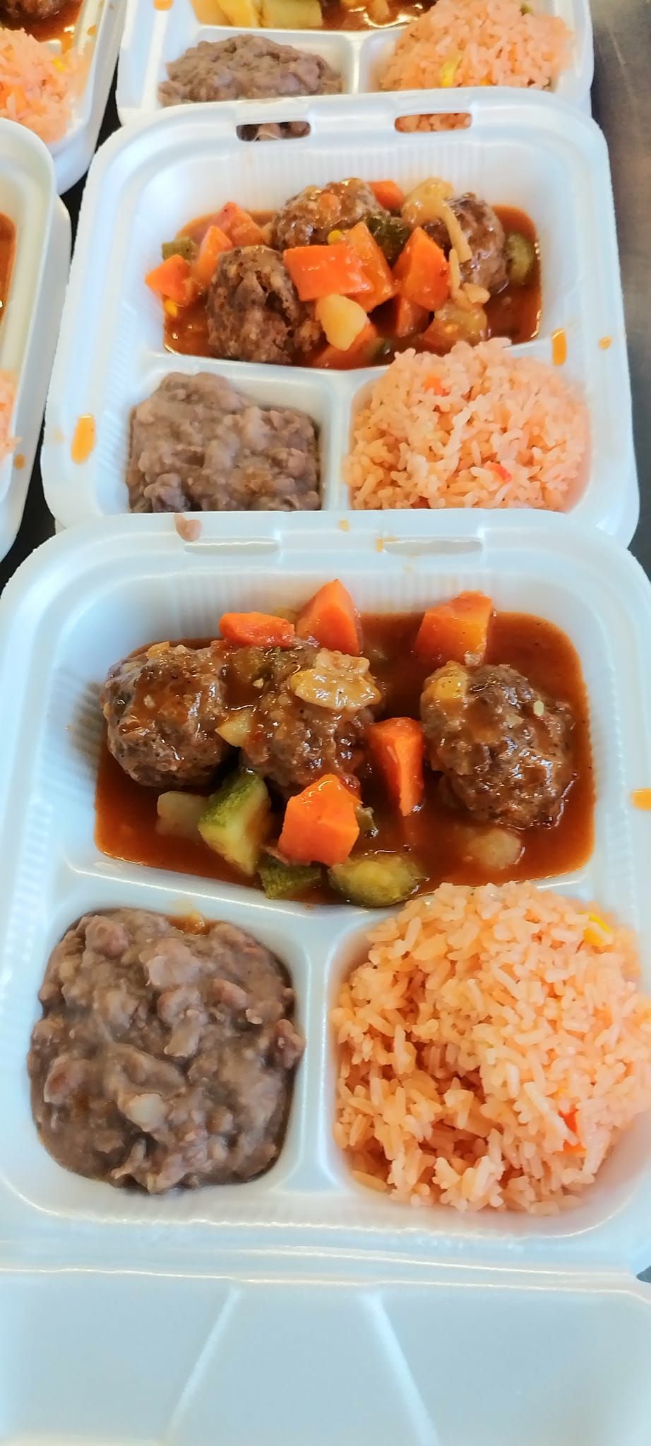 Styrofoam takeout containers each holding meatballs with vegetables, refried beans, and Mexican-style rice.