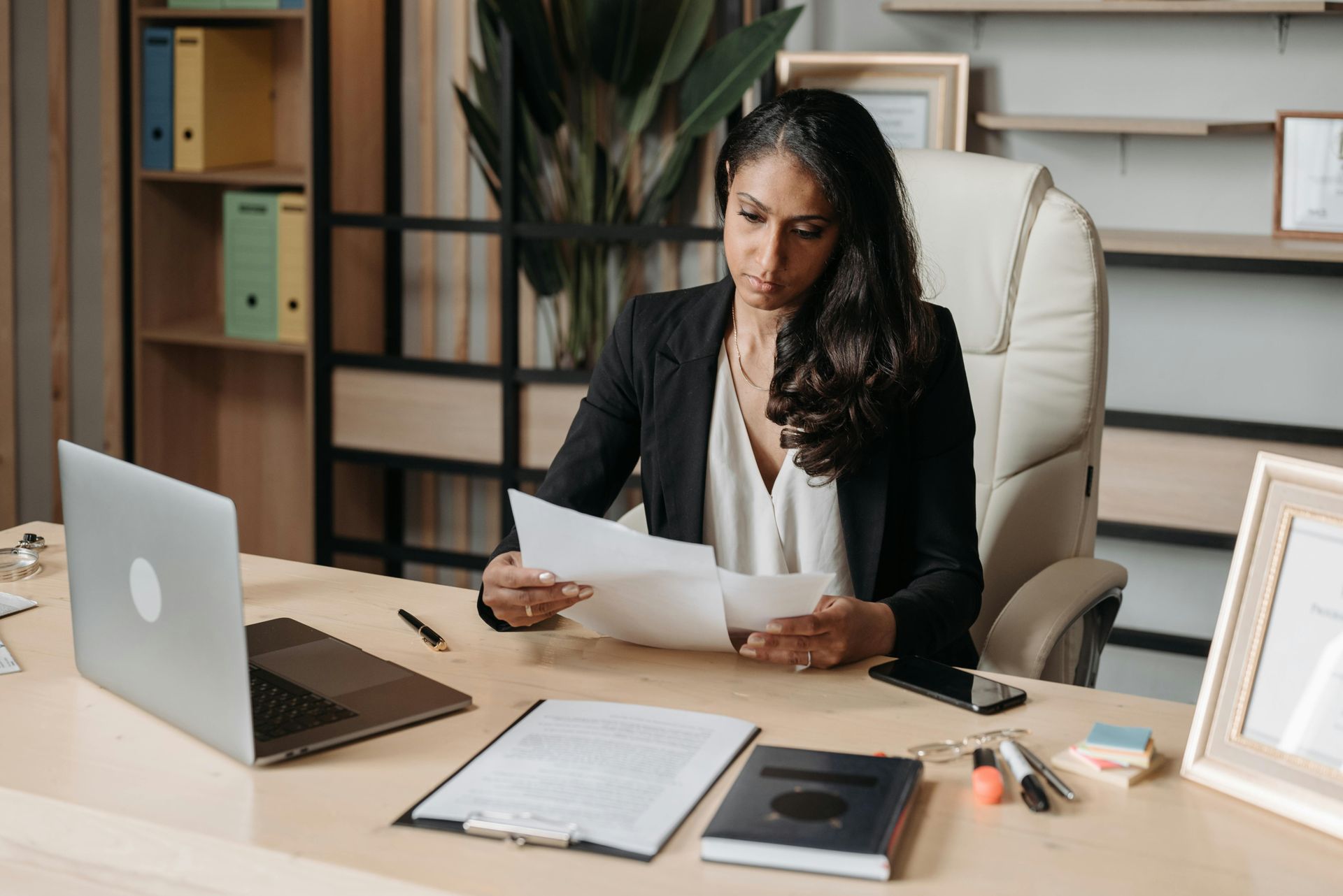 A woman is sitting at a desk with a laptop and a piece of paper.