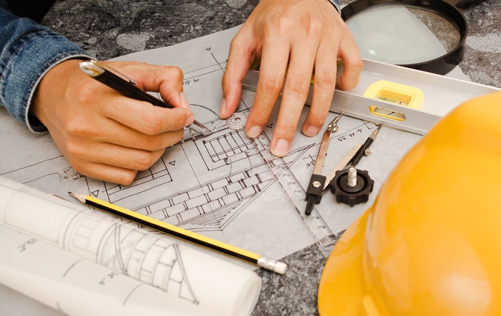 Hands Drawing on Blueprints With Tools — Mid North Coast Drafting & Construction in Nabiac, NSW