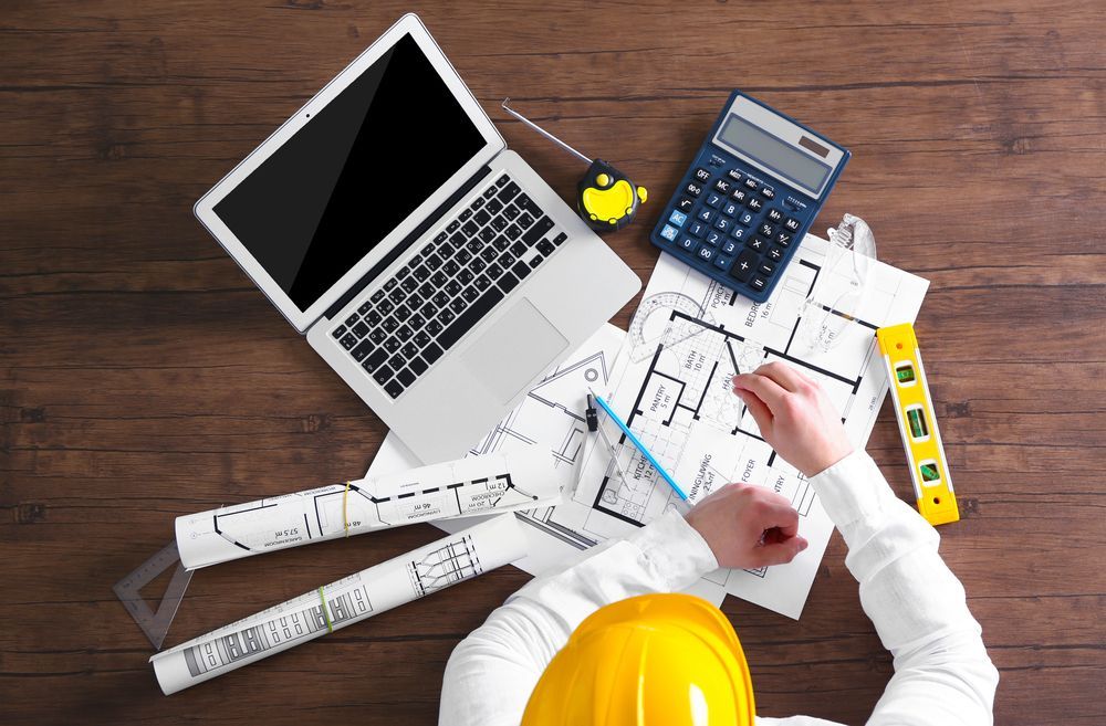 Architect at Work on Blueprints, With Laptop and Calculator — Mid North Coast Drafting & Construction in Wingham, NSW